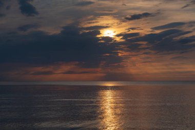 sunset in the sea with clouds and calm water on the surface of which sunlight reflects by creating a light path