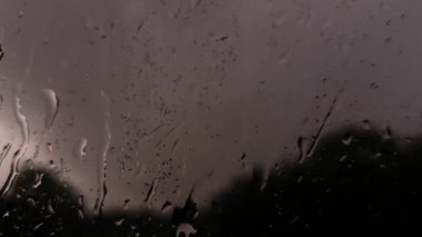 Karanlık bir günde pencereye vuran sağanak yağmurun yakın görüntüsü.