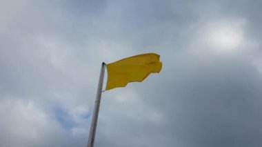 Kumsal uyarısı Bulutlu bir günde rüzgarda dalgalanan sarı bayrak.
