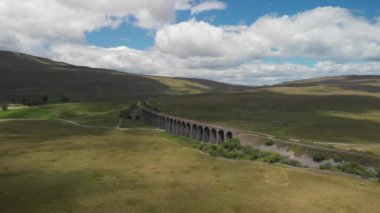 Bu, Cumbria, İngiltere 'deki Ribblehead Viaduct' a doğru giden bir hava görüntüsü. Hava biraz bulutla güneşliydi ve yeşil kırsal bölgeleri en iyi şekilde değerlendirmek için yaz mevsiminde kaydedildi..