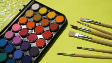 Yeşil arkaplanda boya fırçaları ve suluboya paletleri