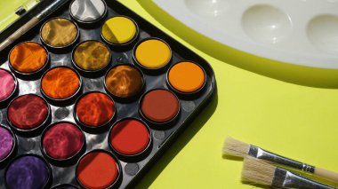 Suluboya paleti ve yeşil arkaplanda boya fırçaları