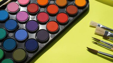 Sarı zemin üzerinde suluboya boya ve fırça seti, üst görünüm