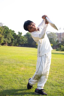 Genç bir çocuk kriket oynarken koruyucu kıyafetiyle vuruyor.