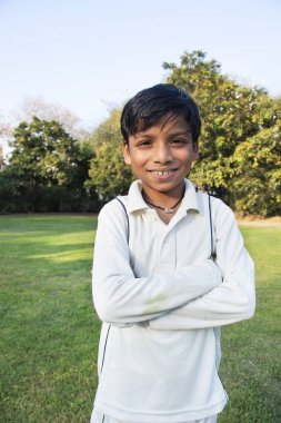 Kriket üniformalı bir çocuk ayakta duruyor.