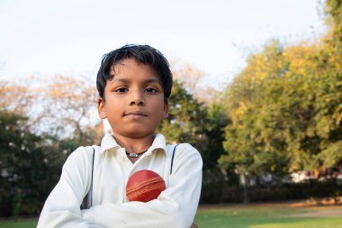 A boy in cricket uniform standing with cricket ball