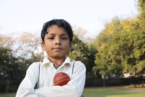A boy in cricket uniform standing with cricket ball