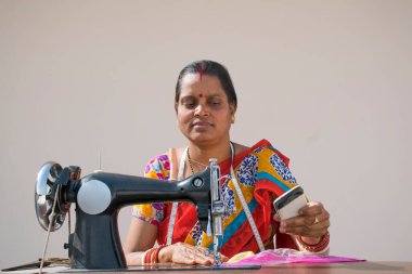 Hintli kadın giysileri makineyle dikiyor ve cep telefonu kullanıyor.