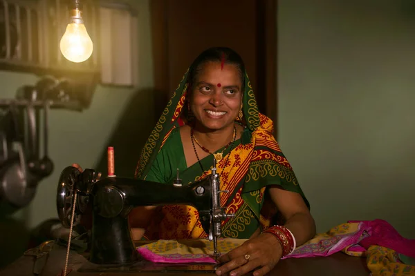 Indian Rural woman stitching clothes by sewing machine at home