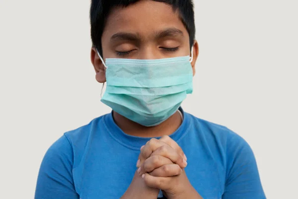 Koronavirüse karşı koruyucu maske takan yakın plan çocuk dua ediyor.