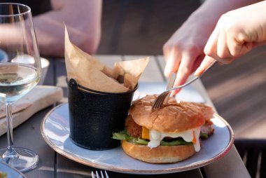 Bir grup arkadaş, restoranda bira ve şarap kadehi kızartıp hamburger yiyorlar. Yetişkinler bir barda hamburger ve içeceklerle