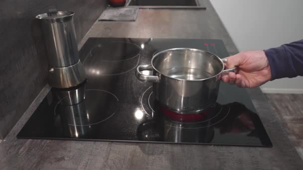 Un uomo mette una pentola d'acqua su una stufa di ceramica per preparare la cena — Video Stock