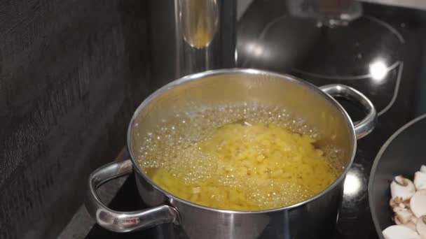 Процесс приготовления пасты. Повар перемешивает макароны в кипящей воде и покрывает крышкой — стоковое видео