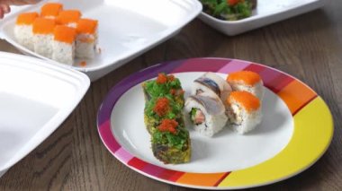 Kadın eli bambu çubuklarını tutuyor ve renkli bir tabakta yemek kabından suşi taşıyor. Yemek servisi.