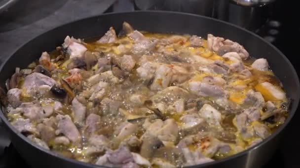 Ένα πιάτο κοτόπουλο, λαχανικά και μανιτάρια βράζει σε ένα τηγάνι γεμάτο σάλτσα. σε κεραμική ηλεκτρική κουζίνα. Μαγειρεύοντας νόστιμα και υγιεινά τρόφιμα. αργή κίνηση — Αρχείο Βίντεο