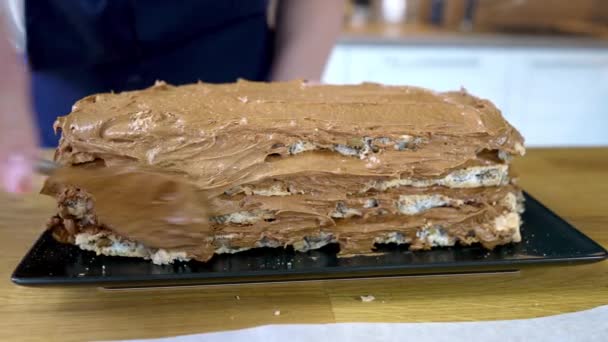 De kok verspreidt chocolademelk op de bovenkant en rond van de meringue cake. Het proces van het maken van een chocoladetaart met noten en room. — Stockvideo