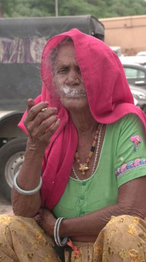 Jaipur, Rajasthan, Hindistan - 11 Ağustos 2019: Tanımlanamayan Hintli yaşlı kadın geleneksel elbiseyle sigara içiyor.