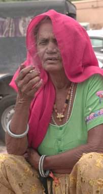 Jaipur, Rajasthan, Hindistan - 11 Ağustos 2019: Tanımlanamayan Hintli yaşlı kadın geleneksel elbiseyle sigara içiyor.