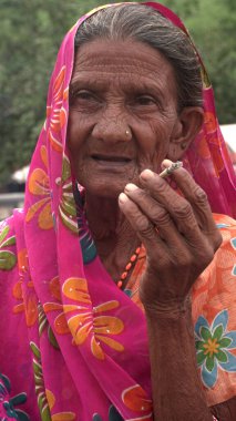 Jaipur, Rajasthan, Hindistan - 11 Ağustos 2019: Tanımlanamayan Hintli yaşlı kadın geleneksel elbiseyle sigara içiyor.