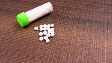 Haplardan oluşan homeopatik ilaçların ve içinde sıvı homeopatik madde bulunan bir şişenin yakın plan görüntüsü..