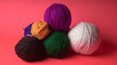 Renkli yün yumakları ve kırmızı bir arka planda sepetteki ahşap iğneler..