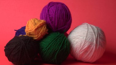 Renkli yün yumakları ve kırmızı bir arka planda sepetteki ahşap iğneler..