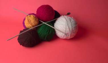 Renkli yün yumakları ve kırmızı bir arka planda sepetteki ahşap iğneler..