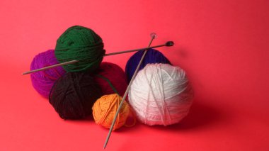 Renkli yün yumakları ve kırmızı bir arka planda sepetteki ahşap iğneler..