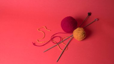 Renkli yün yumakları ve kırmızı bir arka planda sepetteki ahşap iğneler..