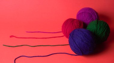 Renkli yün yumakları ve kırmızı bir arka planda sepetteki ahşap iğneler..