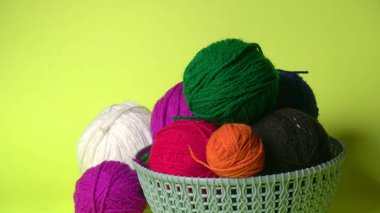 Sarı arka planda renkli yün yumakları ve sepetteki ahşap iğneler..