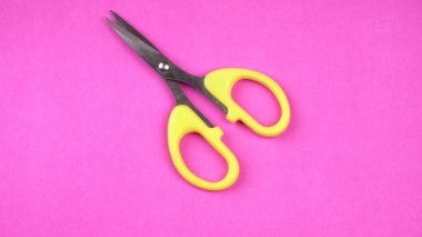 Pembe arka planda sarı makasın üst görüntüsü. Kağıt ve ince malzemeler kesmek için makas kullanılır.