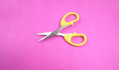 Pembe arka planda sarı makasın üst görüntüsü. Kağıt ve ince malzemeler kesmek için makas kullanılır.