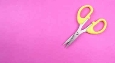 Pembe arka planda sarı makasın üst görüntüsü. Kağıt ve ince malzemeler kesmek için makas kullanılır.