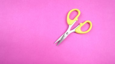 Pembe arka planda sarı makasın üst görüntüsü. Kağıt ve ince malzemeler kesmek için makas kullanılır.