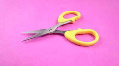 Pembe arka planda sarı makasın üst görüntüsü. Kağıt ve ince malzemeler kesmek için makas kullanılır.