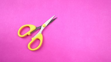 Pembe arka planda sarı makasın üst görüntüsü. Kağıt ve ince malzemeler kesmek için makas kullanılır.