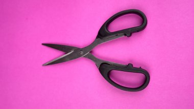 Pembe arka planda izole edilmiş siyah makasın üst görüntüsü. Kağıt ve ince malzemeler kesmek için makas kullanılır.