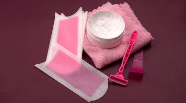 Renkli havluyla kadın derisini güvenle tıraş etmek için balmumu şeritleri, krema kavanozu ve pembe kullan-at tıraş bıçakları, kadın saçı temizleme konsepti.