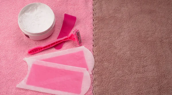 Closeup of wax strips with jar of cream and pink disposable razors for safe shaving of female skin on colorful towel, female hair removal concept