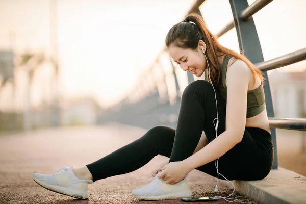 Spor giyimli güzel Asyalı kadınlar gün batımında parkta egzersiz yaparken müzik dinliyorlar. Sağlıklı kadın kavramı.