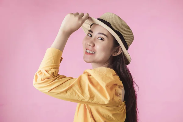 Portrait of young asian woman smiling in summer dress and hat standing on pink background. Beautiful girl with copy space