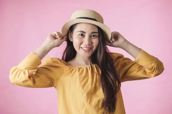 Portrait of young asian woman smiling in summer dress and hat standing on pink background. Beautiful girl with copy space