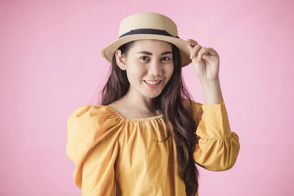 Portrait of young asian woman smiling in summer dress and hat standing on pink background. Beautiful girl with copy space