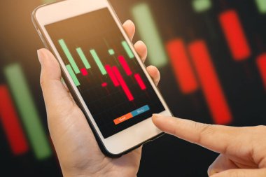 Finansal hisse senedi verileri ve parmaklarıyla akıllı telefondan alım satımı kontrol ediliyor.