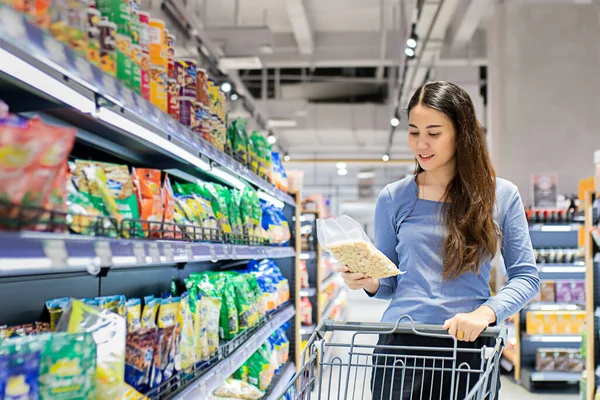 Güzel genç Asyalı kadın süpermarkette alışveriş arabası itiyor. Alışveriş süpermarketi konsepti.