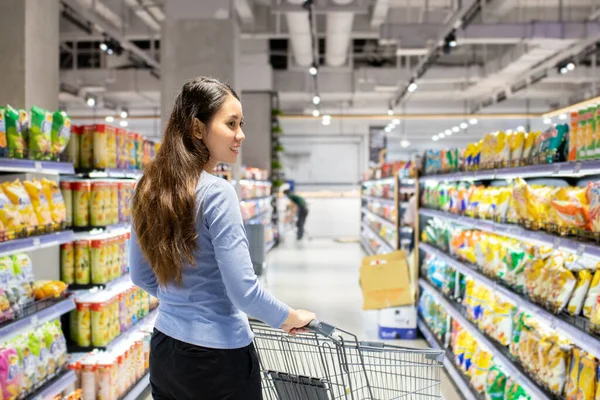 Güzel genç Asyalı kadın süpermarkette alışveriş arabası itiyor. Alışveriş süpermarketi konsepti.