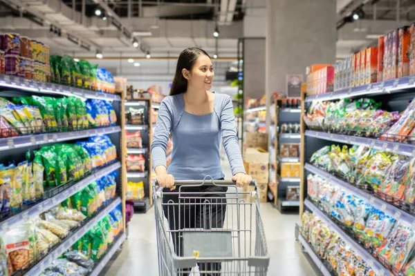 Güzel genç Asyalı kadın süpermarkette alışveriş arabası itiyor. Alışveriş süpermarketi konsepti.