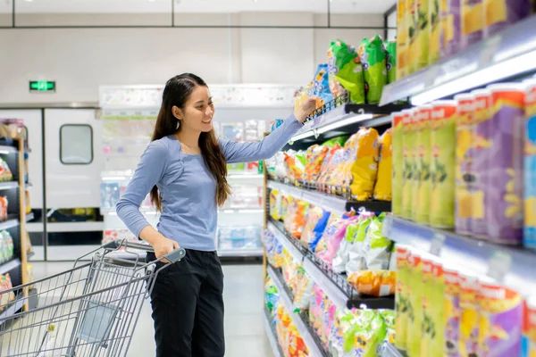 Güzel genç Asyalı kadın süpermarkette alışveriş arabası itiyor. Alışveriş süpermarketi konsepti.