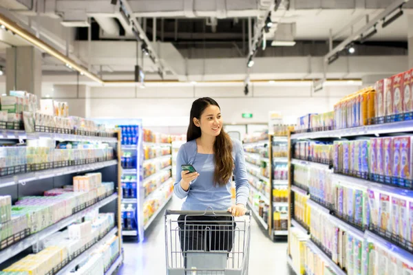 Güzel genç Asyalı kadın süpermarkette alışveriş arabası itiyor. Alışveriş süpermarketi konsepti.